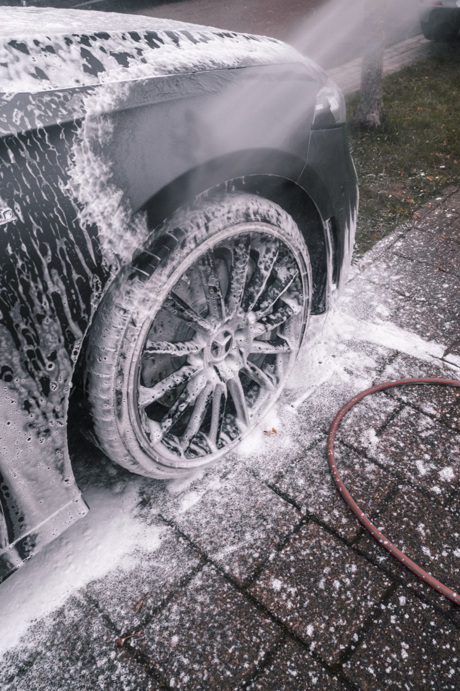 A dark car and its wheel completely covered in thick white foam
